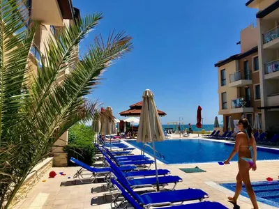 a woman walking past a row of lounge chairs by a pool at Obzor Beach Resort Apartment G-109 in Obzor