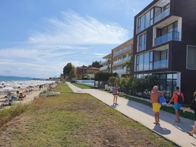 a group of people walking down a sidewalk next to the beach at Апартамент За Гости ,,ХРИСТИНА