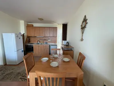a kitchen with a wooden table with chairs and a white refrigerator at Sea Fort Club & Grand Resort in Sveti Vlas