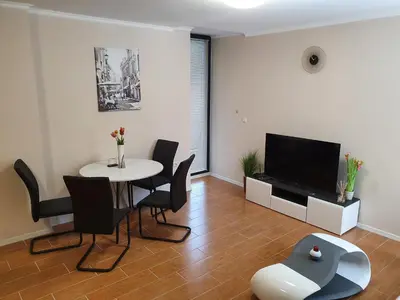 a living room with a table and chairs and a television at Апартамент За Гости ,,1В-15