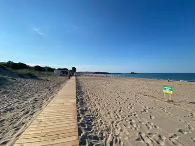 a boardwalk on a beach with a sign in the sand at Студио Симона 3 - първа линия море in Lozenets