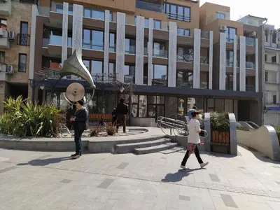 two people walking in a courtyard in front of a building at Top center apartment Gramophone with private parking in Burgas City