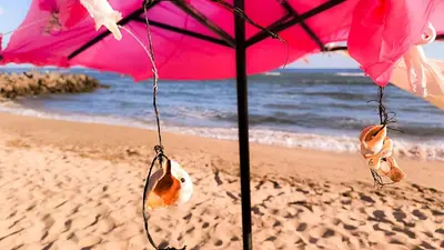 a pink umbrella on the beach with some shoes at William's apartments - second cozy studio in Sveti Vlas