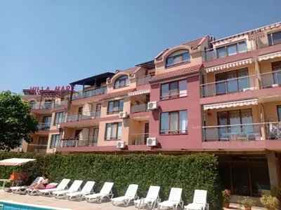 a large pink building with lounge chairs next to a pool at Апартамент на къмпинг Градина in Chernomorets