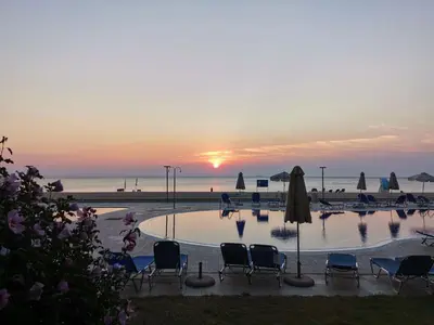 a pool with chairs and umbrellas and the ocean at sunset at Апартамент Б003 в Обзор Бийч Резорт- море пред прозореца, плаж пред вратата !!! in Obzor