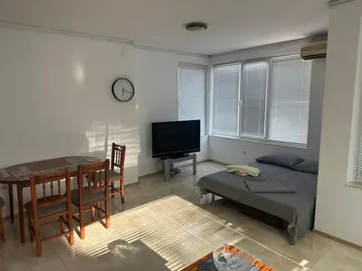 a living room with a bed and a table and a tv at Апартамент Енигма in Sveti Vlas