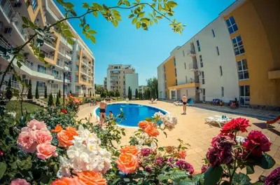 a courtyard with a pool with flowers and buildings at Fort Noks - Menada Apartments in Sveti Vlas