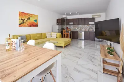 a living room with a yellow couch and a kitchen at Luxury First Line apartment with pool by the sea in Nesebar