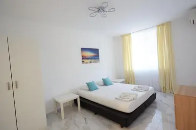 a white bedroom with a bed and a window at Luxury First Line apartment with pool by the sea in Nesebar