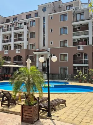 a pool with benches and a palm tree in front of a building at Apartment Casa del Mar (Dinevi Resort) in Sveti Vlas