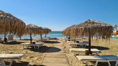 a row of straw umbrellas and chairs on a beach at Sun Wave Apartament in Sveti Vlas