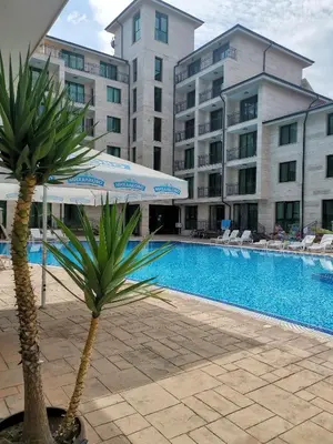 a palm tree and an umbrella next to a swimming pool at Lovely Apartments Amadeus Lux in Sunny Beach