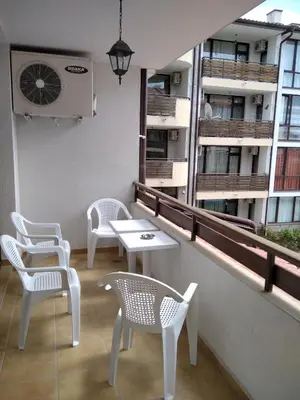 a balcony with white chairs and tables and a building at Victoria's apartments Nesebar in Nesebar