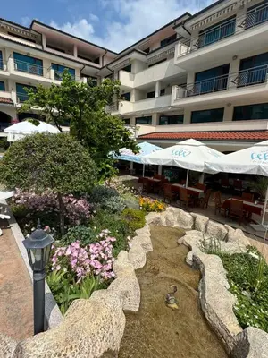 a garden in front of a hotel with tables and umbrellas at Cozy 1 bed apartment in Lesso Complex (Ravda, Nessebar) in Ravda