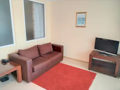 a living room with a brown couch and a flat screen tv at Апартамент Сънсет Ризорт in Pomorie
