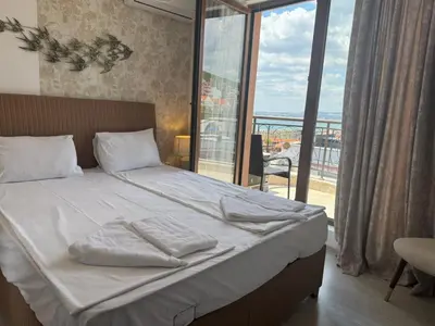 a bedroom with a bed with white sheets and a balcony at Fenix Apart Complex in Sveti Vlas