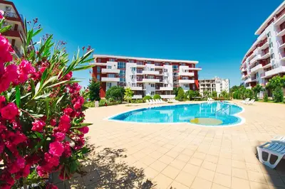 a swimming pool in front of a building with pink flowers at Panorama Fort Beach in Sveti Vlas