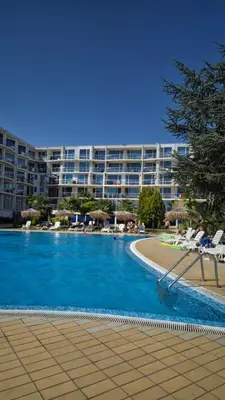 a large swimming pool with chairs and a large building at Apartment with green terrace in Burgas City