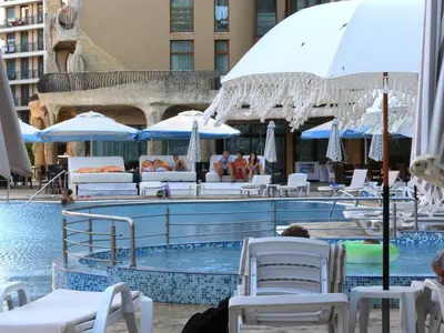 a swimming pool with white chairs and umbrellas at Sunrise Studio Grenada in Sunny Beach