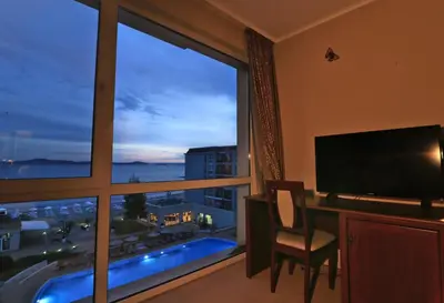 a room with a large window with a desk and a television at Първа линия Апартаменти in Pomorie