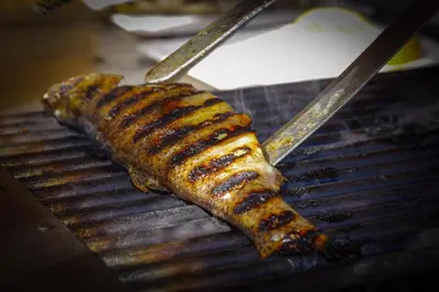 a grill with two tongs and a grilled sausage at Рибарник Forest Мagic in Topolitsa