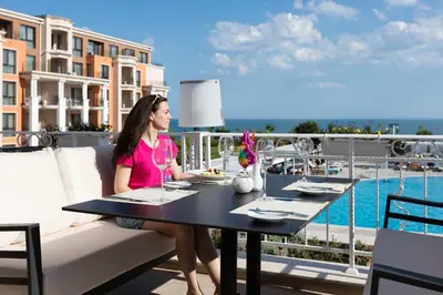 a woman sitting at a table on a balcony at Premier Fort Beach Hotel in Sveti Vlas