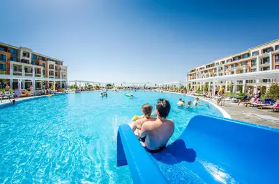 a man and child sitting on the edge of a pool at a resort at Premier Fort Beach Resort in Sunny Beach