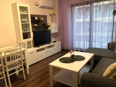 a living room with a couch and a tv and a table at Purple Rose Apartment Valencia Gardens in Nesebar