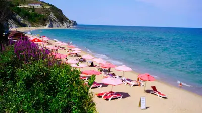 a beach with pink umbrellas and chairs and the ocean at Byala Cliff Sea View Suite in Byala