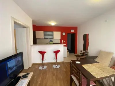 a living room with a table and a kitchen with red walls at VIOLET GARDEN 2 Veranda Apartment in Sunny Beach