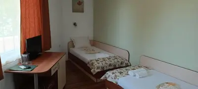 a small room with two beds and a desk at Семеен Хотел Детелини in Primorsko