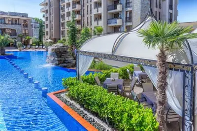 a swimming pool with chairs and palm trees in a resort at Солнечный берег Grand Kamelia in Sunny Beach