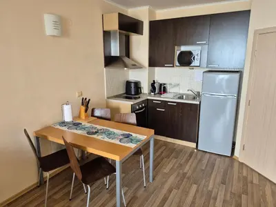 a kitchen with a wooden table with chairs and a refrigerator at Апартамент Б306 в Обзор Бийч Резорт на първа линия с перфектен изглед към плажа! in Obzor